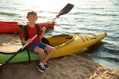 Photo of Happy boy with paddle sitting on kayak near river. Summer camp activity