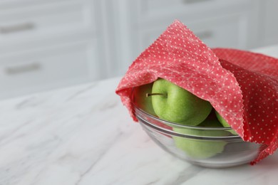 Photo of Apples in bowl covered with beeswax food wrap on white table, closeup. Space for text