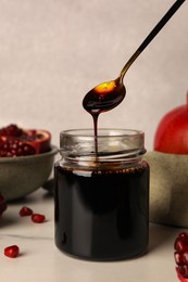 Photo of Spoon with tasty pomegranate sauce over glass jar at white marble table