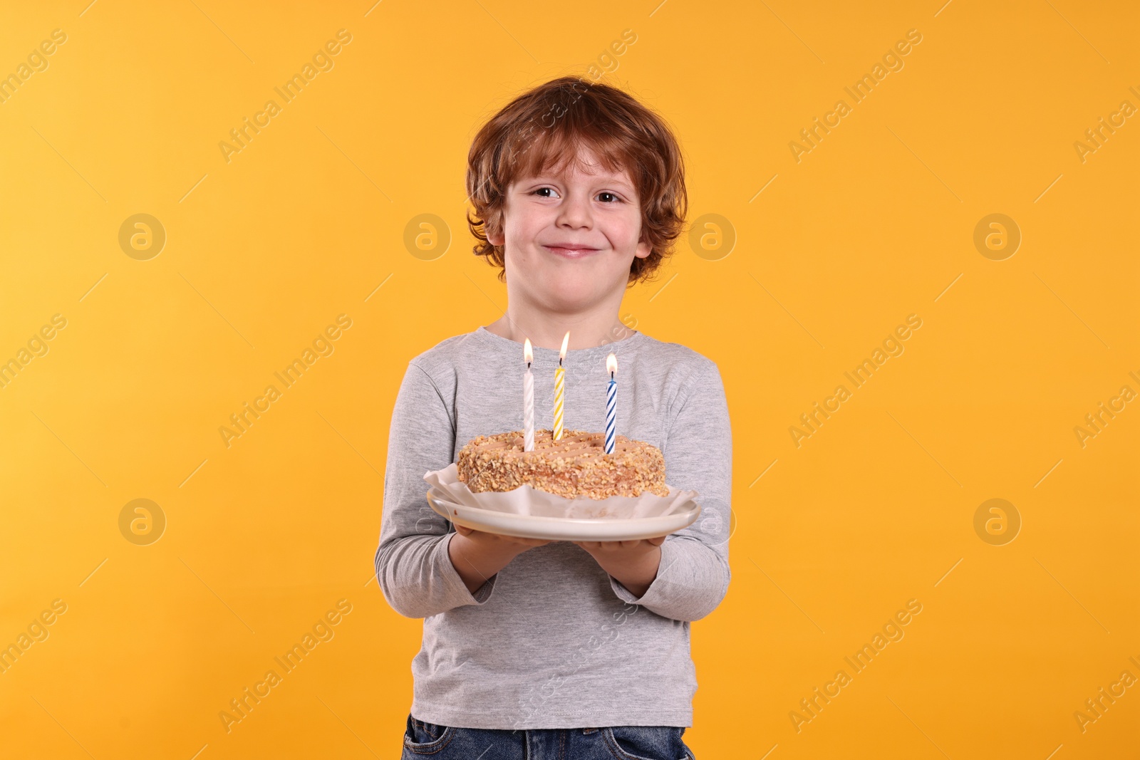 Photo of Birthday celebration. Cute little boy holding tasty cake with burning candles on orange background