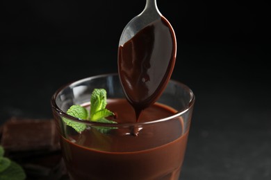 Photo of Taking delicious hot chocolate with spoon on dark background, closeup