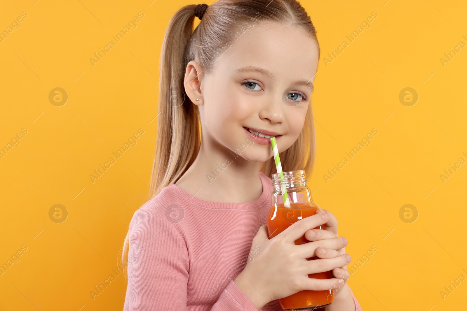 Photo of Cute little girl drinking fresh juice on orange background