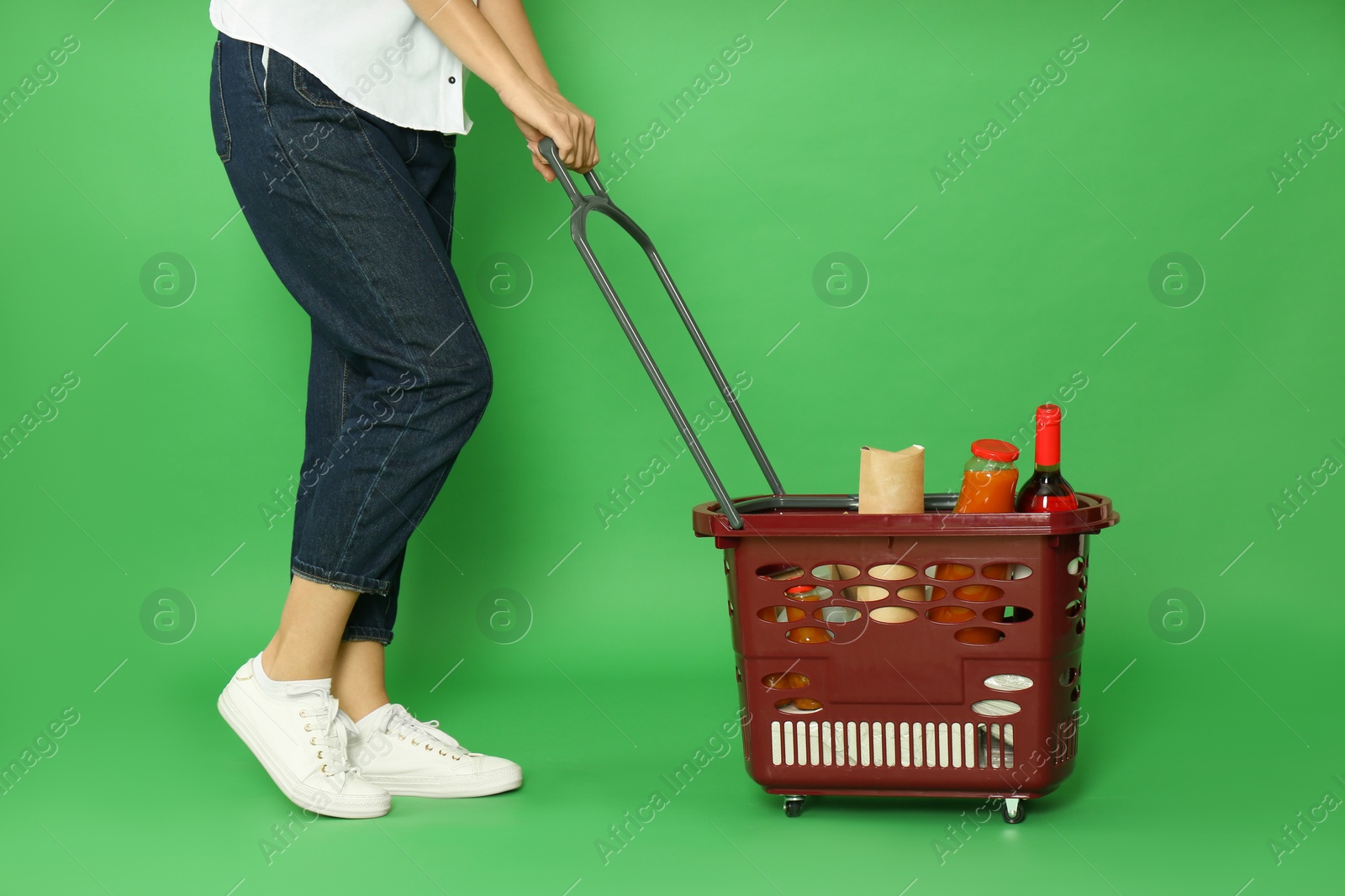 Photo of Woman with shopping basket full of different products on green background, closeup