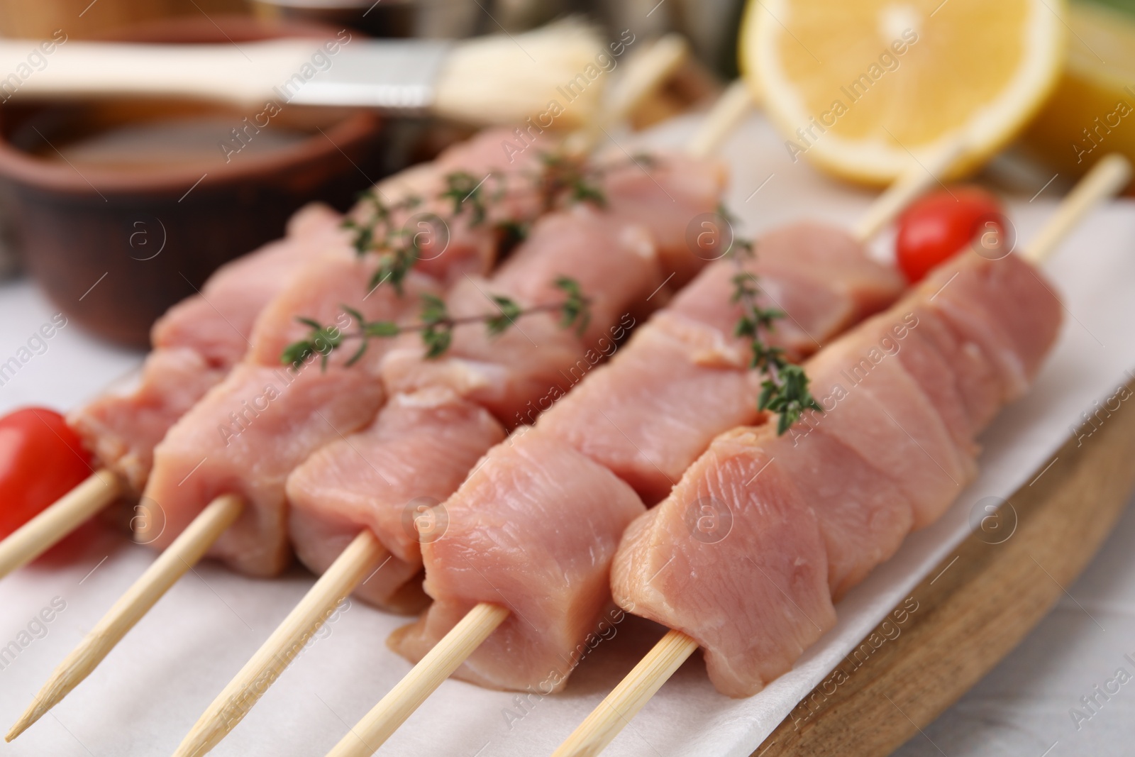 Photo of Skewers with cut raw meat, thyme and tomatoes on table, closeup