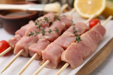 Skewers with cut raw meat, thyme and tomatoes on table, closeup