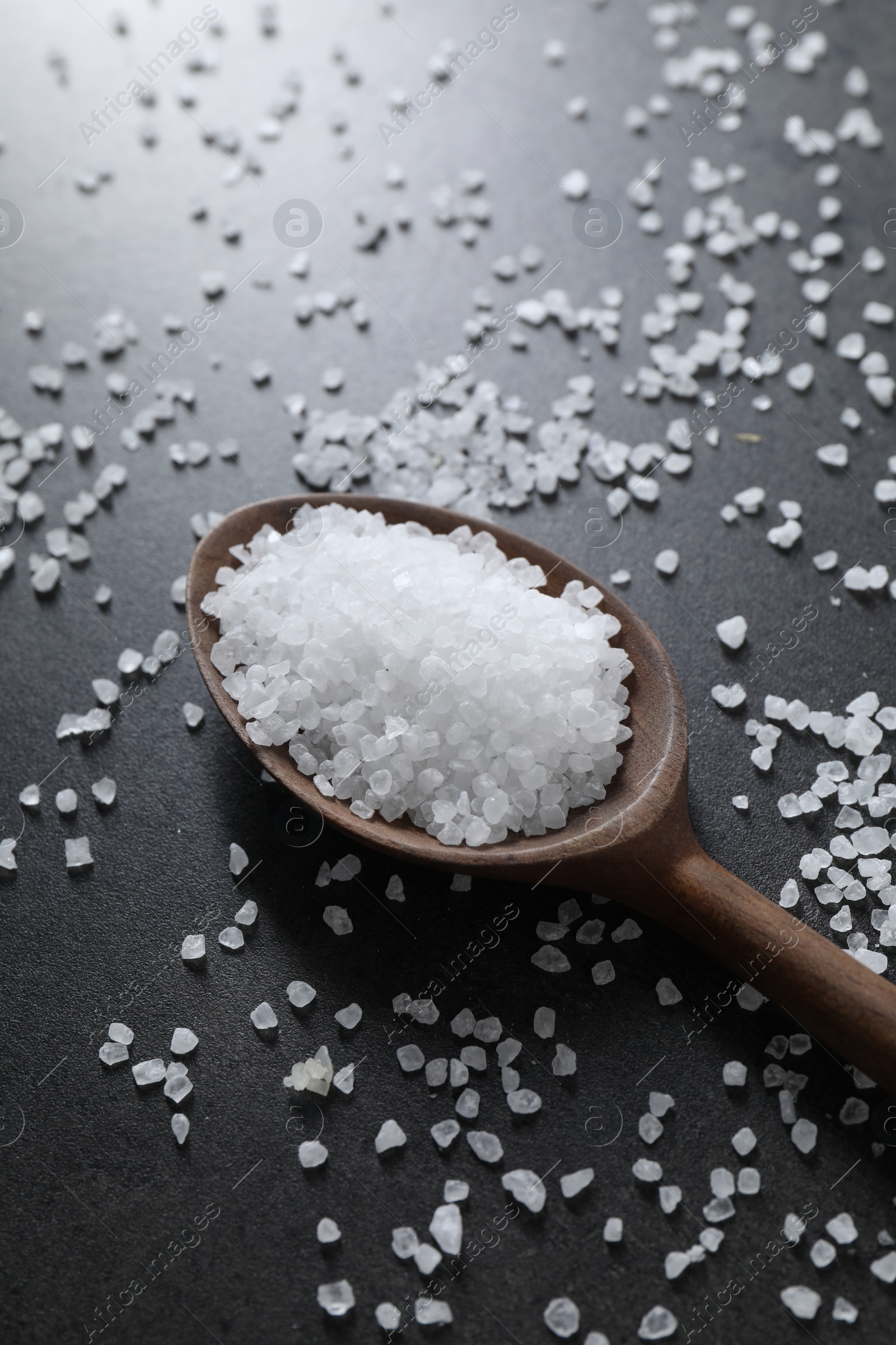 Photo of Natural salt and wooden spoon on black table