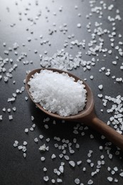 Photo of Natural salt and wooden spoon on black table