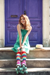 Beautiful girl with retro roller skates sitting on stairs near violet door