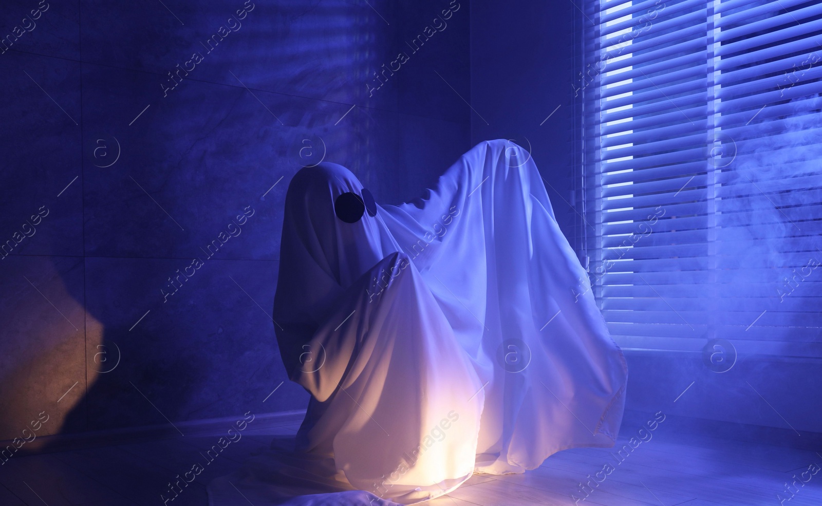 Photo of Creepy ghost. Woman covered with sheet near window in blue light