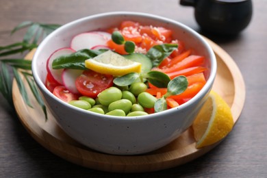 Poke bowl with salmon, edamame beans and vegetables on wooden table, closeup