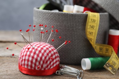 Photo of Checkered pincushion with pins and other sewing tools on wooden table