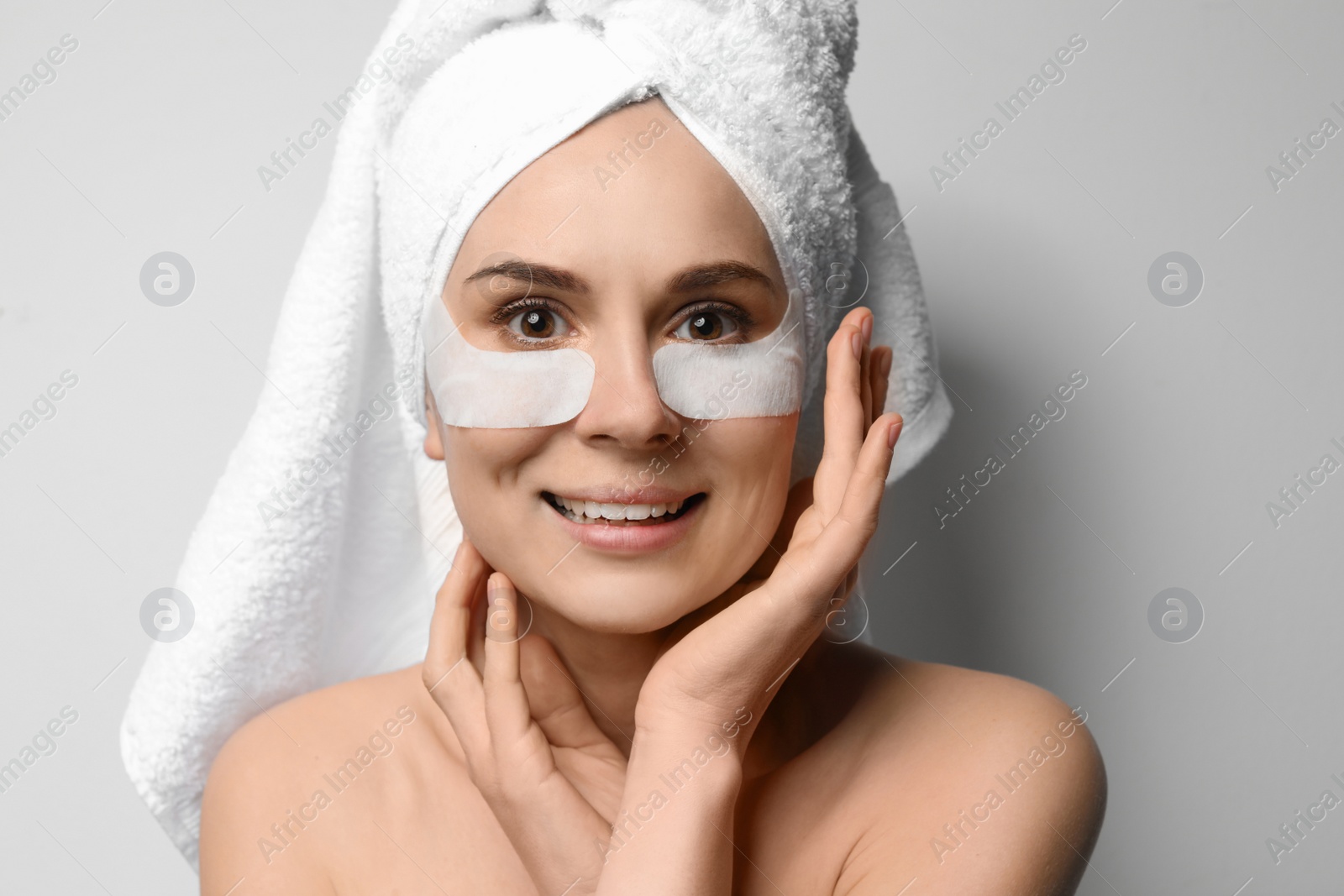 Photo of Beautiful woman with eye patches against light background. Facial mask