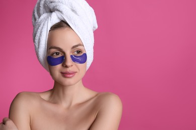 Photo of Beautiful young woman with under eye patches and hair wrapped in towel on pink background, space for text