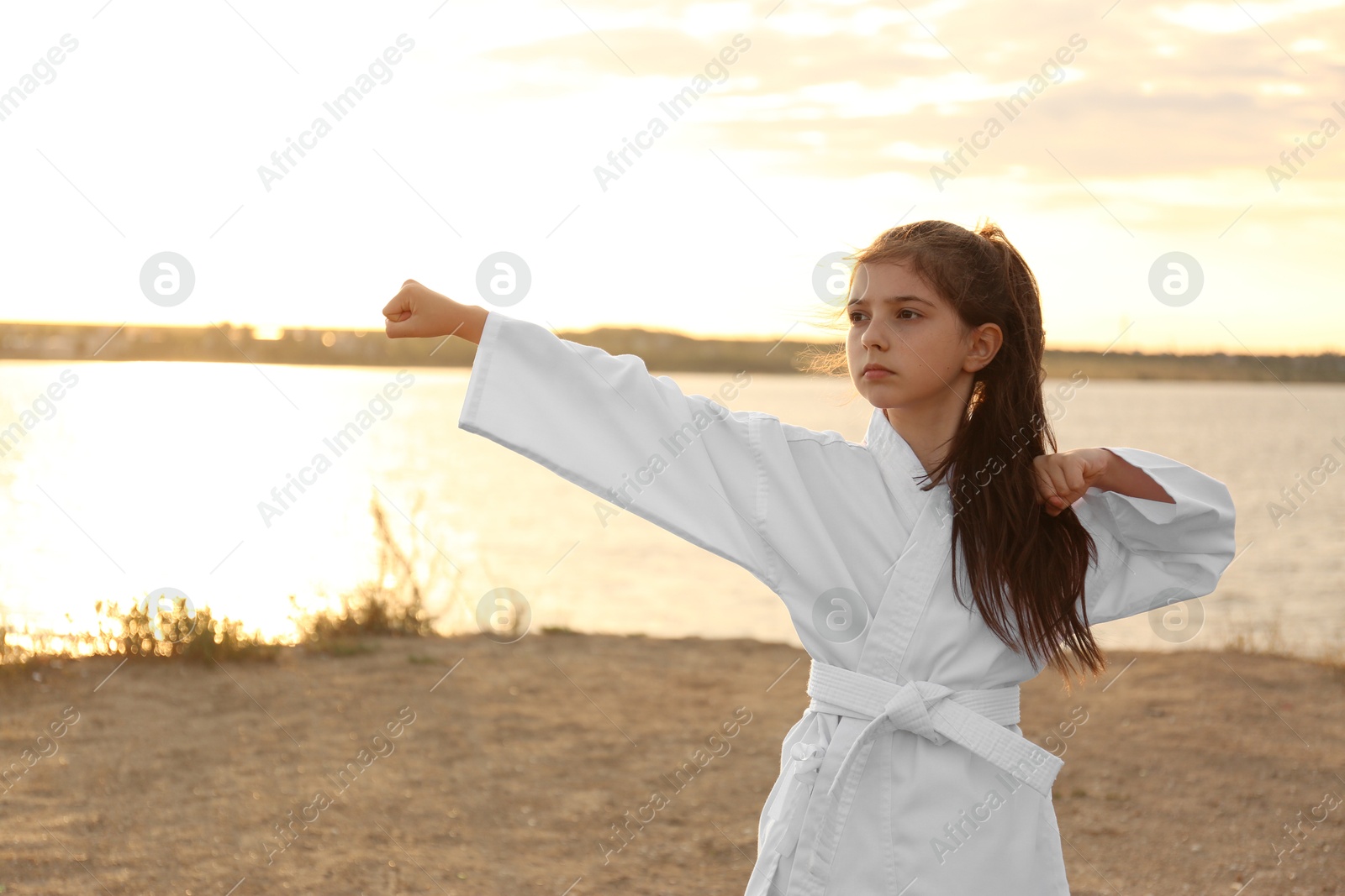 Photo of Cute little girl in kimono practicing karate near river at sunset