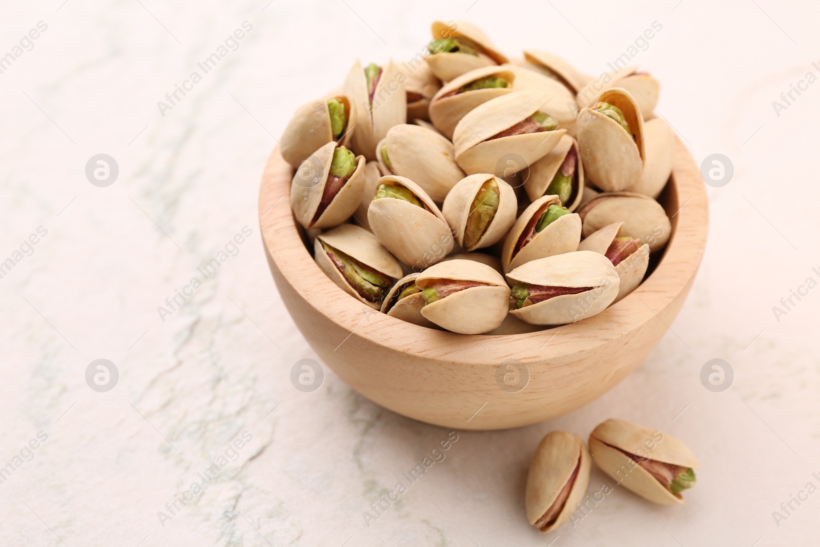 Photo of Delicious pistachios in bowl on white textured table