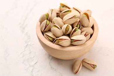 Photo of Delicious pistachios in bowl on white textured table