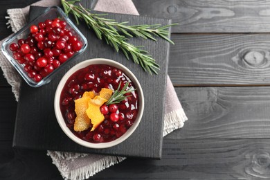 Photo of Fresh cranberry sauce, rosemary, orange peel and berries on black wooden table, top view. Space for text