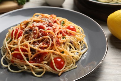 Delicious pasta with anchovies, tomatoes and parmesan cheese served on white wooden table, closeup