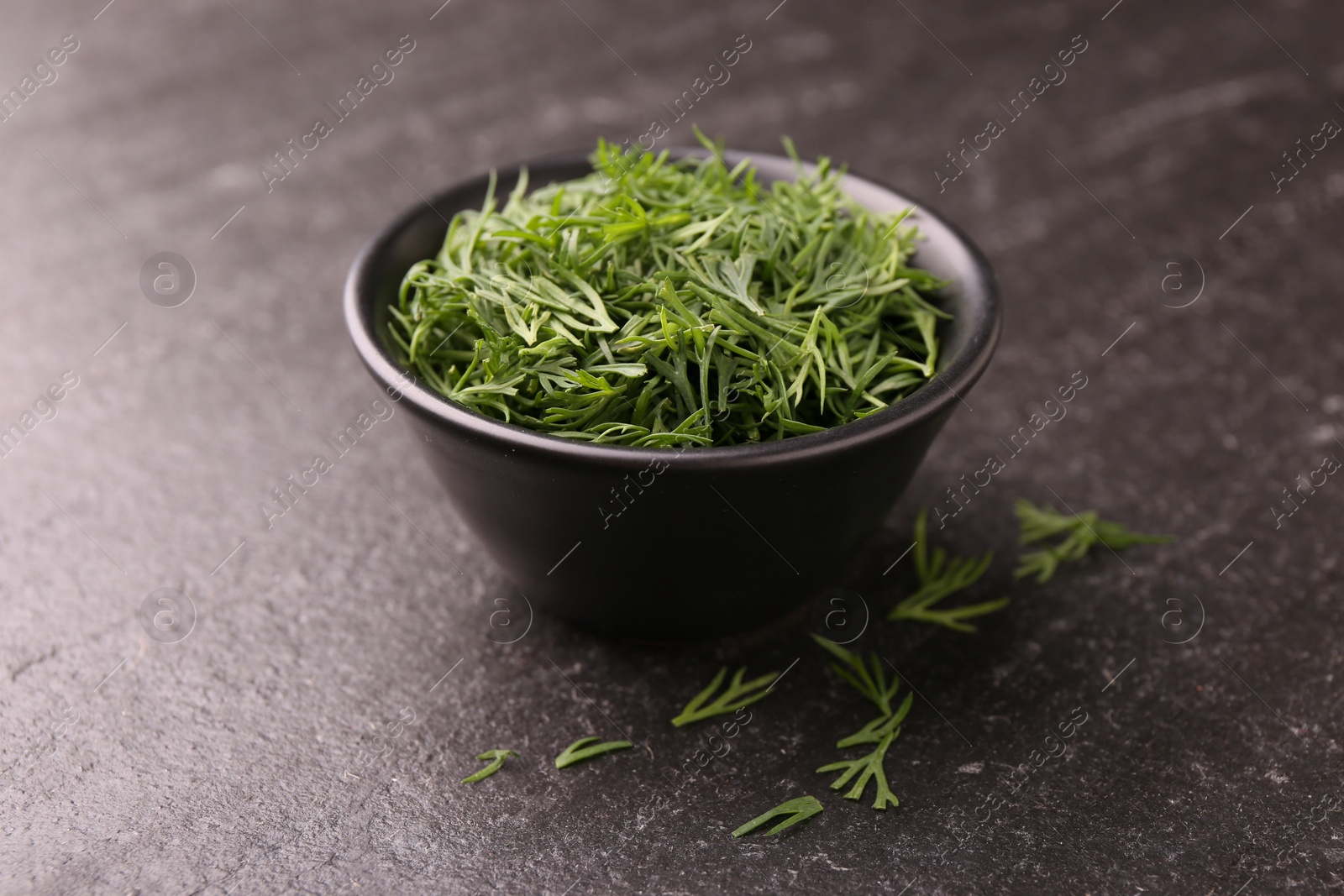 Photo of Fresh cut dill in bowl on dark textured table, closeup