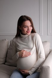 Photo of Young pregnant woman sitting on sofa at home