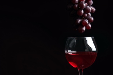 Photo of Fresh ripe juicy grapes over glass with red wine and space for text on black background