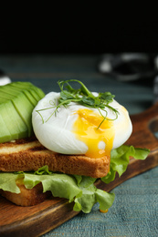 Photo of Delicious poached egg with toasted bread and avocado served on wooden board, closeup