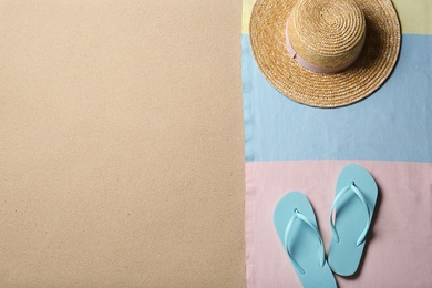 Photo of Straw hat, flip flops and space for text on beach sand, top view. Summer vacation