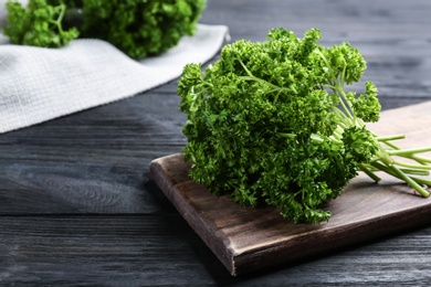 Fresh curly parsley and cutting board on black wooden table. Space for text