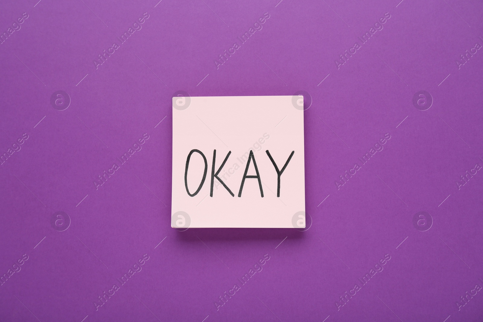 Photo of Note with word Okay on purple background, top view