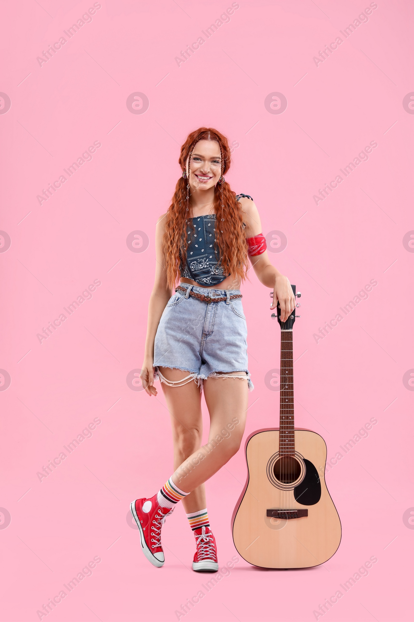 Photo of Stylish young hippie woman with guitar on pink background