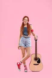 Photo of Stylish young hippie woman with guitar on pink background