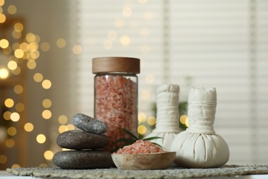 Photo of Spa composition. Herbal bags, sea salt and stones on table indoors, bokeh effect