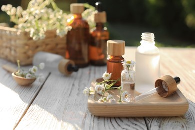 Chamomile essential oil, pipette and flowers on white wooden table outdoors, space for text