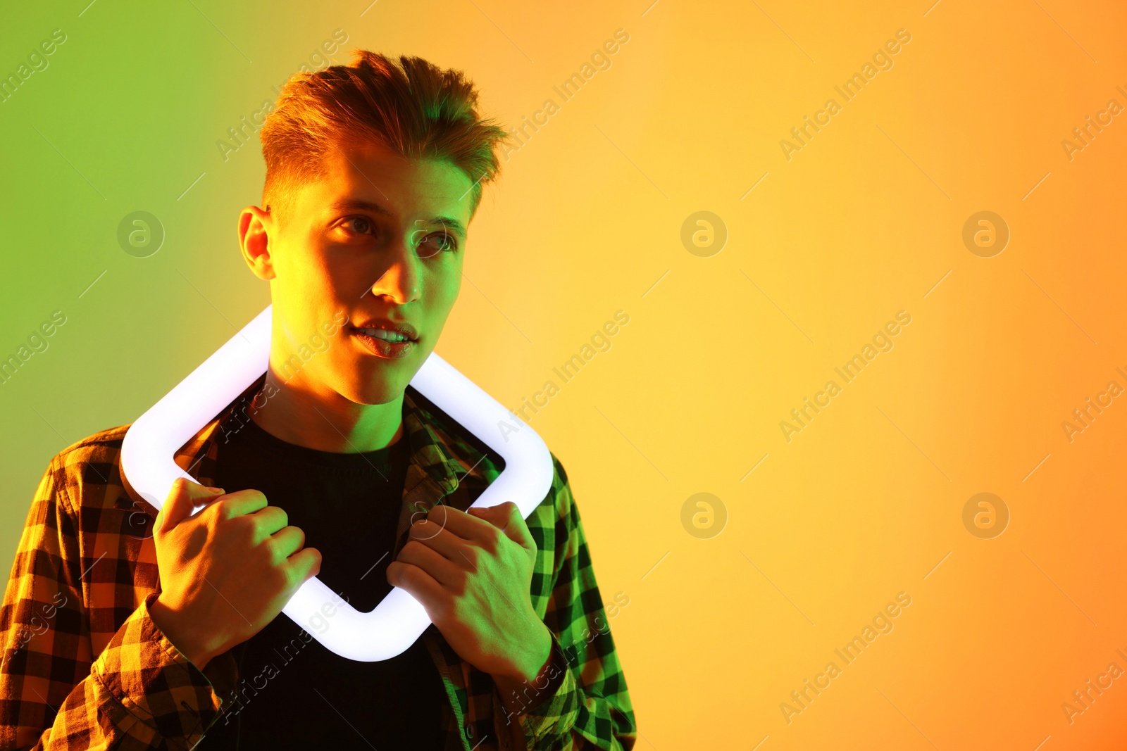 Photo of Young man with square lamp on color background in neon lights. Space for text