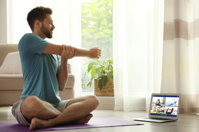 Image of Distance yoga course during coronavirus pandemic. Man having online video class via laptop at home