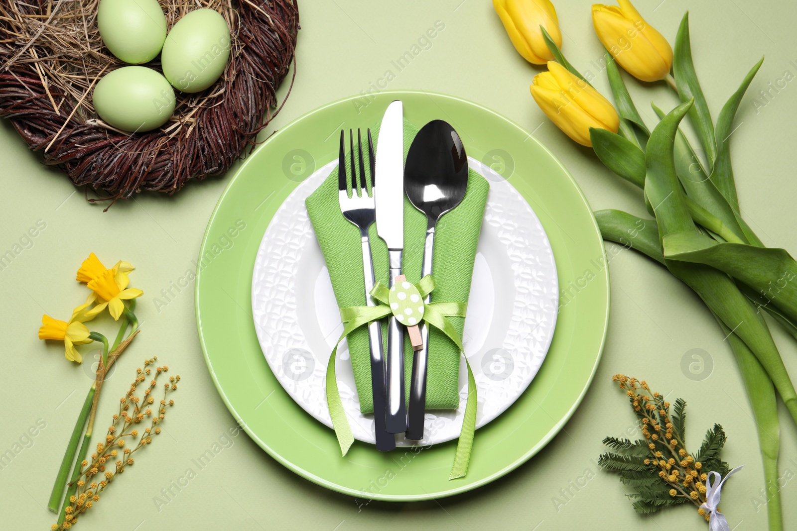 Photo of Festive Easter table setting with eggs on light green background, flat lay