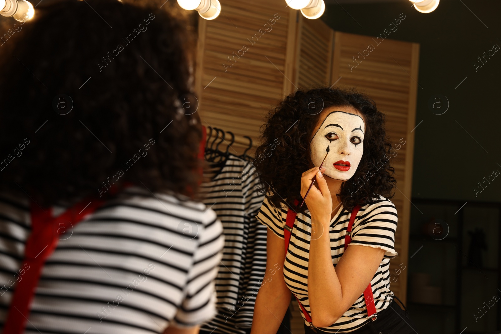 Photo of Young woman applying mime makeup near mirror indoors