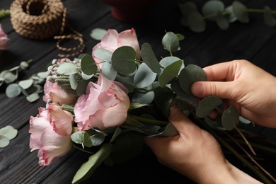 Photo of Florist creating beautiful bouquet at black wooden table, closeup