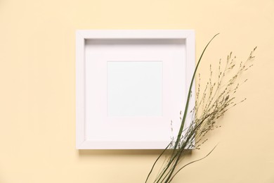 Photo of Empty photo frame and wild flowers on beige background, flat lay. Space for design