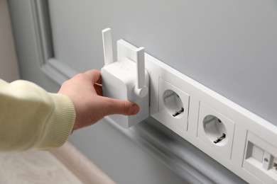 Woman turning on wireless Wi-Fi repeater indoors, closeup