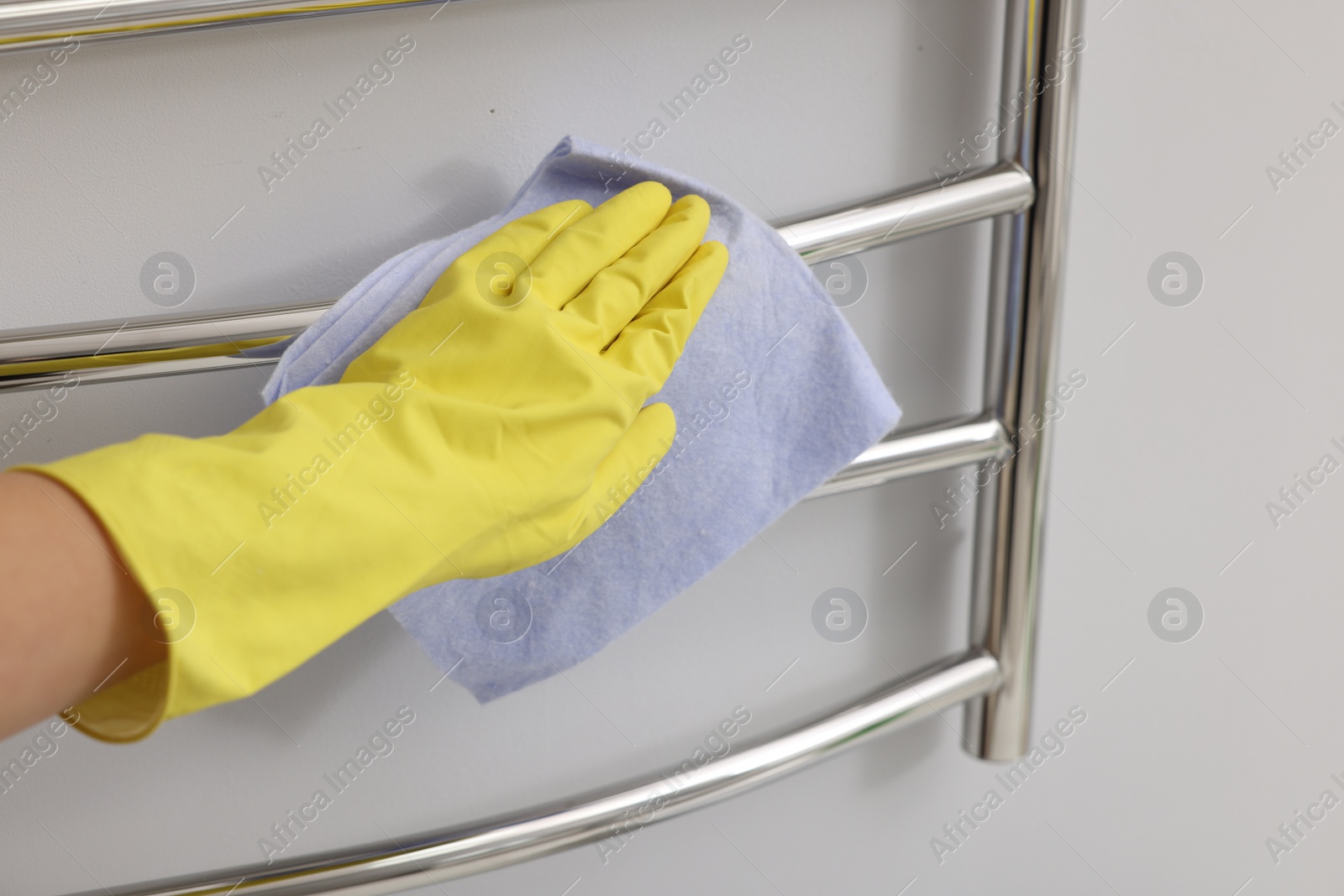 Photo of Woman cleaning heated towel rail with rag indoors, closeup