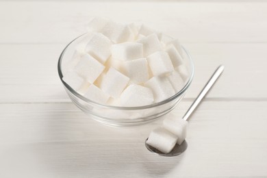 Bowl with sugar cubes and spoon on white wooden table