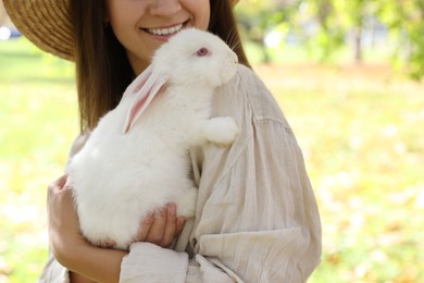 Photo of Happy woman holding cute white rabbit in park, closeup