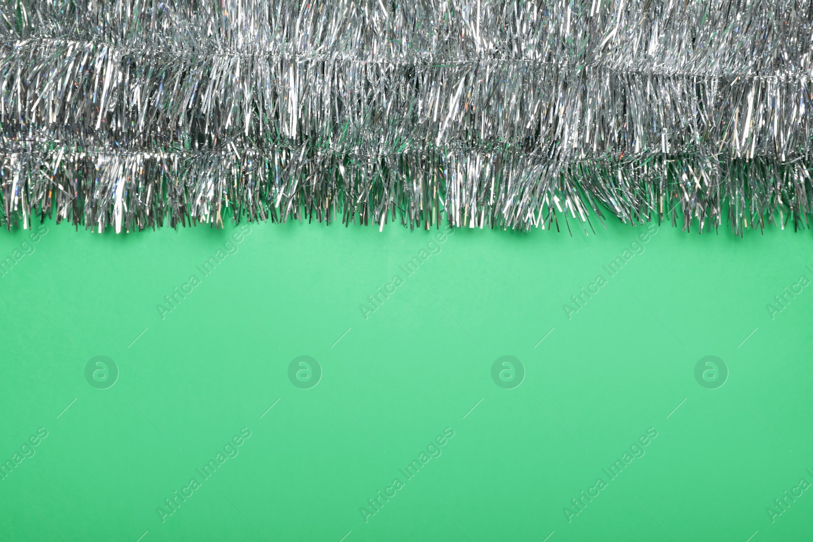 Photo of Silver tinsel on green background, top view. Space for text