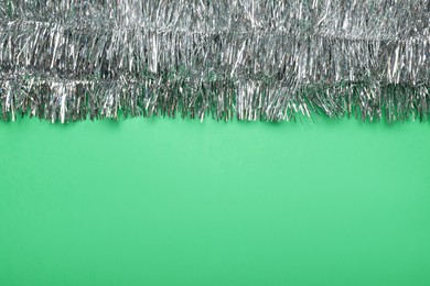 Silver tinsel on green background, top view. Space for text
