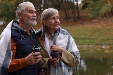 Photo of Affectionate senior couple with cups of coffee in autumn park, space for text