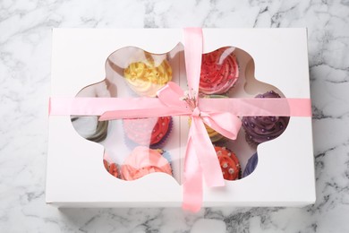Photo of Different colorful cupcakes in box on white marble table, top view