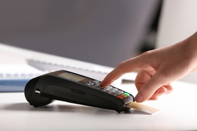 Woman using modern payment terminal at table indoors, closeup. Space for text