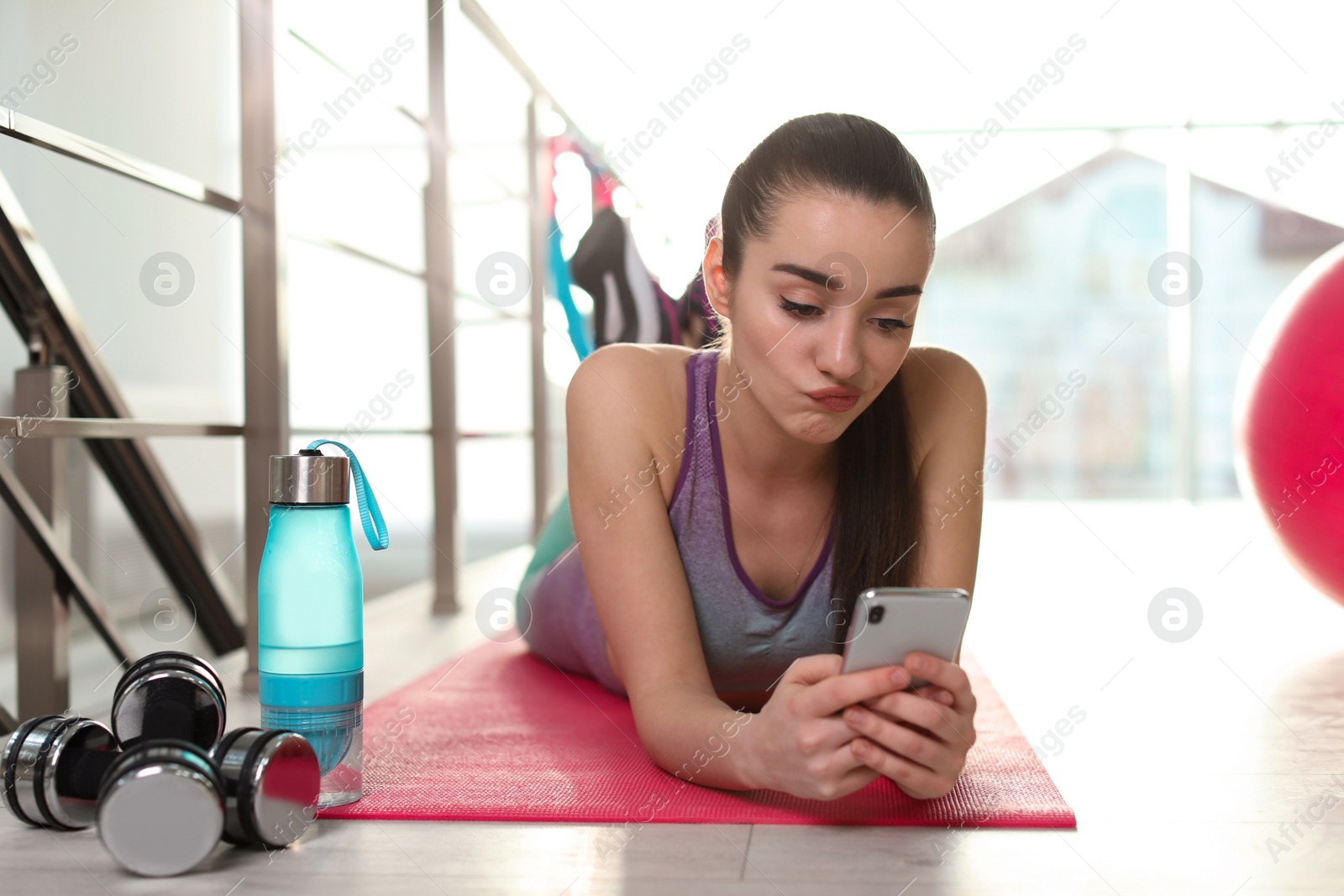 Photo of Lazy young woman with smartphone on yoga mat indoors