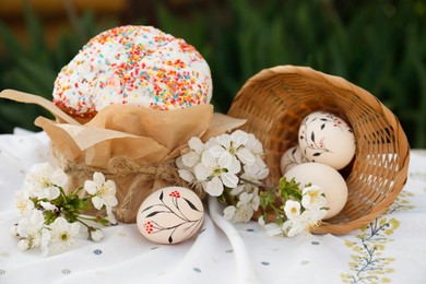 Photo of Eggs with floral ornaments and kulich for Easter near blossoming tree twigs on cloth
